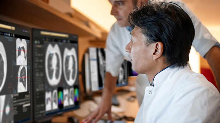 Two medical professionals look at diagnostic results on a series of monitors