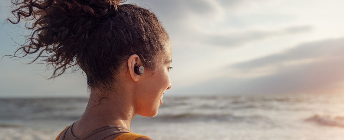 Γυναίκα που χρησιμοποιεί πραγματικά ασύρματα ακουστικά στην παραλία